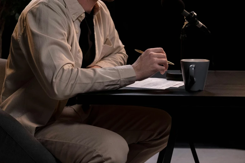 a man sitting at a table in front of a microphone, by Gavin Hamilton, set design, lie detector test, ignant, writing a letter