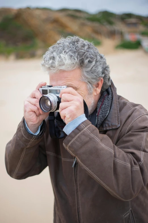 a man taking a picture with a camera, by Peter Churcher, on beach, lovingly looking at camera, telephoto, fujifilm x100v