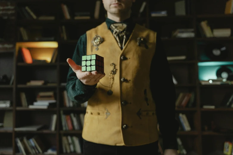 a man standing in front of a bookshelf holding a rubik cube, inspired by Ernő Rubik, unsplash, surrealism, wearing elaborate green and gold, victorian alchemists, live-action archival footage, cinematic outfit photo