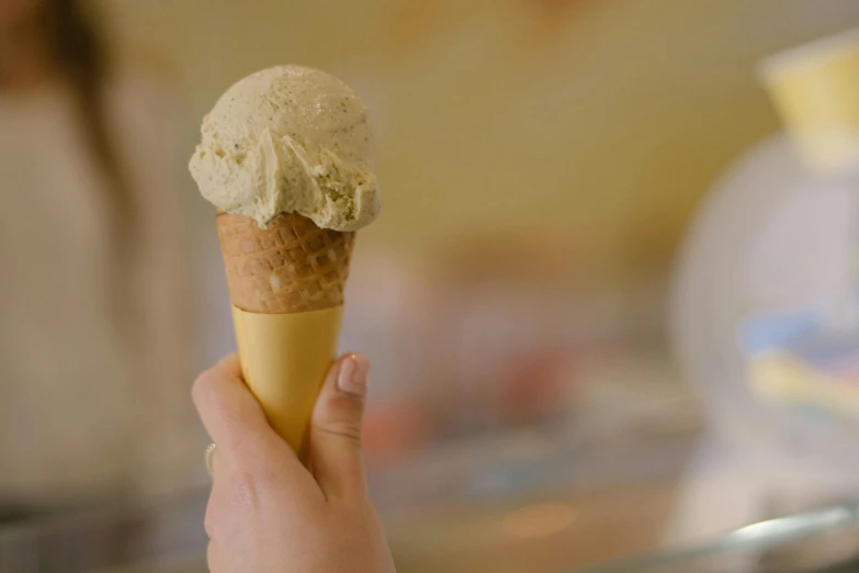 a person holding an ice cream cone in their hand, by Jessie Algie, trending on pexels, renaissance, beige cream natural muted tones, food commercial 4 k, golden, manuka