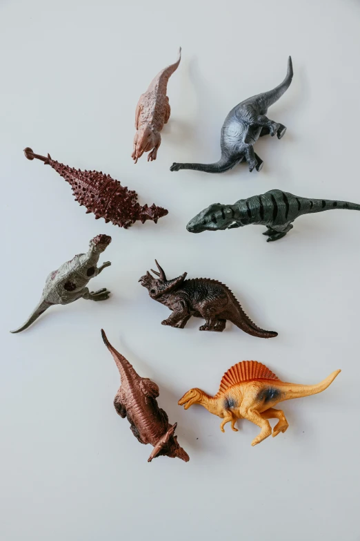 a group of toy dinosaurs sitting on top of a white surface, by Jessie Algie, trending on unsplash, kinetic art, wall art, mineral collections, group of seven, made of plastic