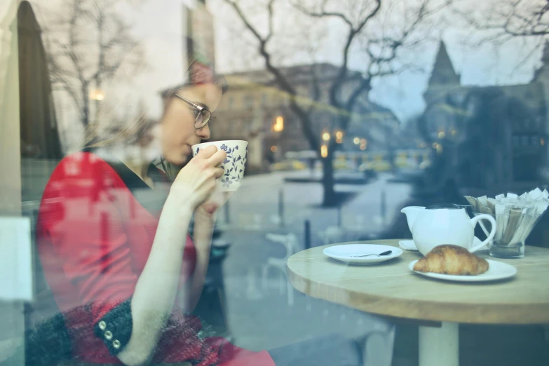 a woman sitting at a table with a cup of coffee, by Zofia Stryjenska, pexels contest winner, romanticism, square, looking through frosted glass, eating outside, high resolution