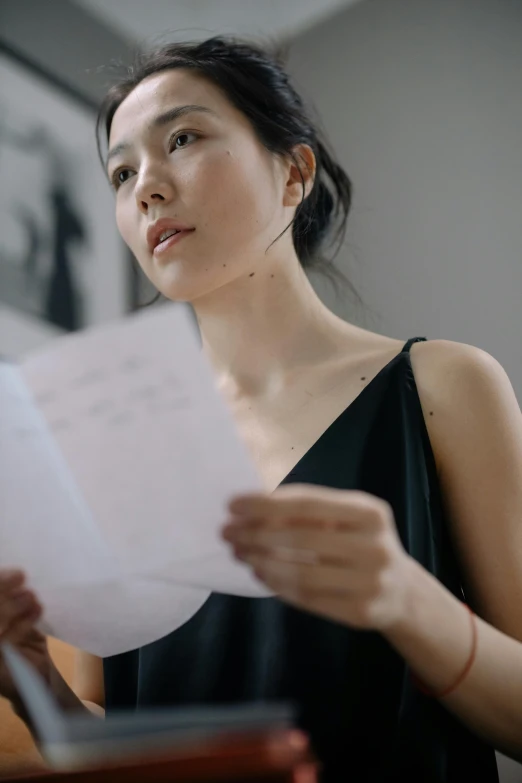 a woman in a black dress holding a piece of paper, by Mei Qing, pexels contest winner, detailed expression, song nan li, bare shoulders, reading