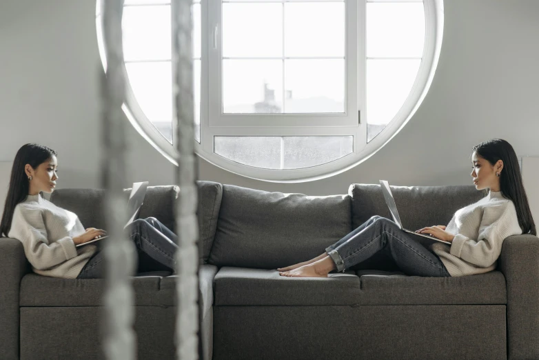 a woman sitting on a couch using a laptop, by Adam Marczyński, pexels contest winner, minimalism, two girls, cracked windows, panoramic centered view of girl, low - angle shot