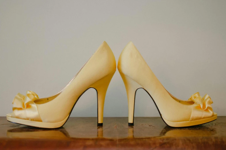 a pair of shoes sitting on top of a wooden table, yellow makeup, standing elegantly, commercially ready, flirting