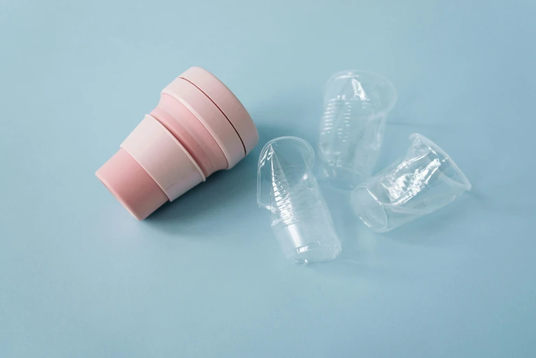 a couple of plastic cups sitting on top of a blue surface, light pink, incubator medpods, clear curvy details, set against a white background