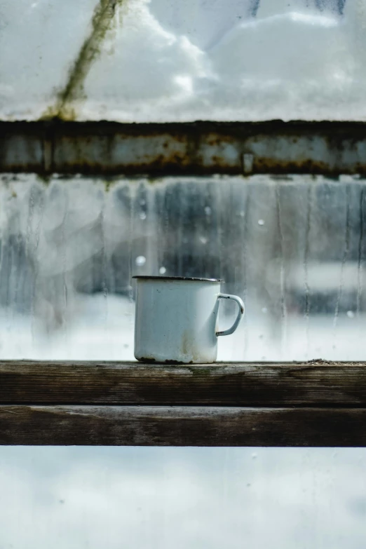 a cup of coffee sitting on a window sill, inspired by Elsa Bleda, pexels contest winner, minimalism, rusted junk, snowing, mug shot, low quality photo