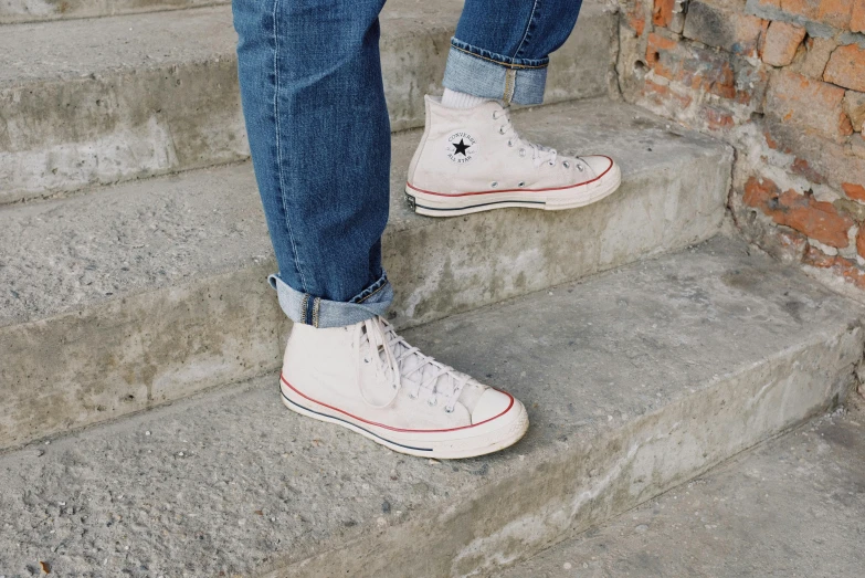 a person standing on some steps with a skateboard, wearing red converse shoes, cream, wearing denim, zoomed out shot