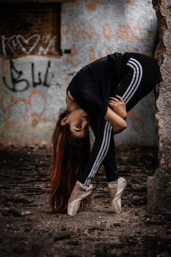 a woman doing a handstand in front of a wall, an album cover, inspired by Elizabeth Polunin, pexels contest winner, wearing a tracksuit, dilapidated look, profile image, focused photo