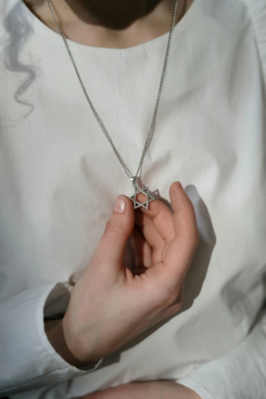 a close up of a person holding a necklace, by Nina Hamnett, hebrew, star inside, lightweight, small