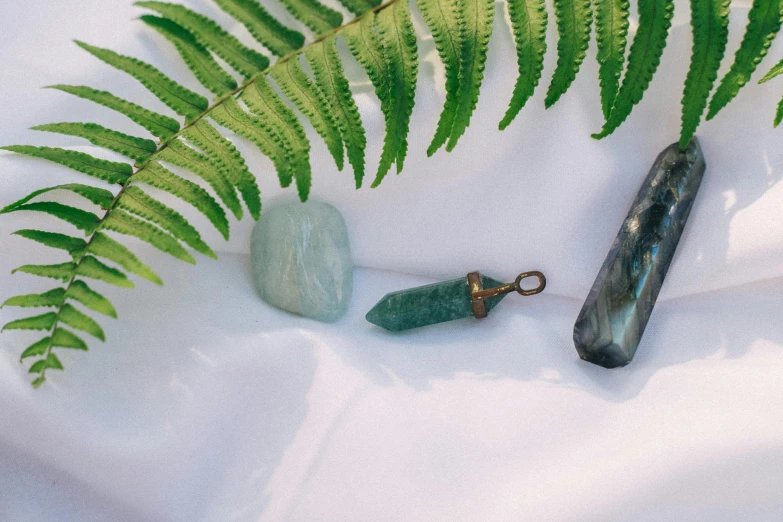 a couple of green stones sitting on top of a white sheet, a still life, inspired by Eden Box, trending on pexels, moonstone, various items, pendants, shop window for magical weapons