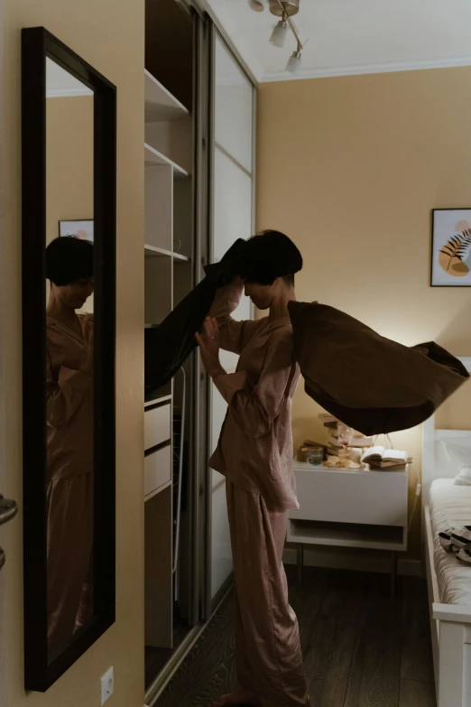 a woman that is standing in front of a mirror, a picture, inspired by Itō Shinsui, pexels contest winner, hotel room, waving robe movement, medium format. soft light, brown and pink color scheme