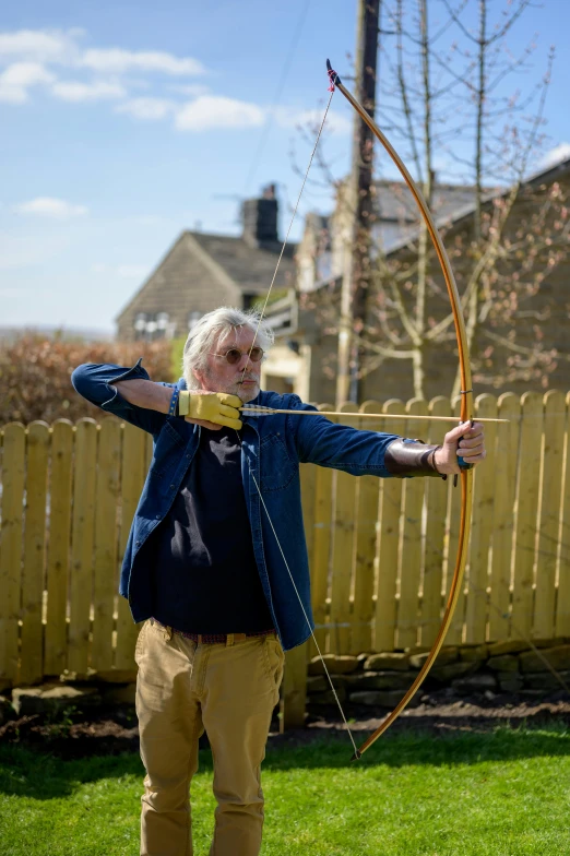a man that is standing in the grass with a bow, by Peter Churcher, pulling the move'derp banshee ', ebony wood bow, yorkshire, photographed for reuters