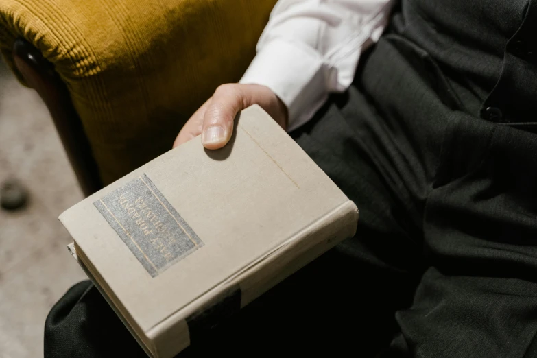 a close up of a person holding a book, dapper, rectangle, sitting down casually, old book