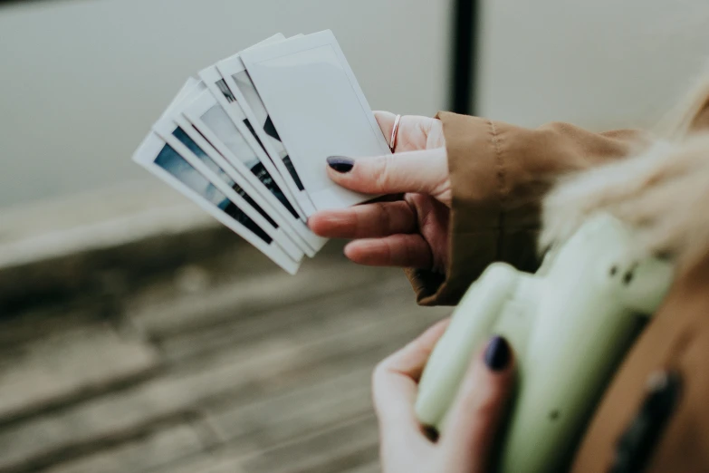 a woman holding a bunch of cards in her hand, a polaroid photo, by Daniel Lieske, pexels contest winner, trade card game, glossy white, outdoor photo, high angle close up shot