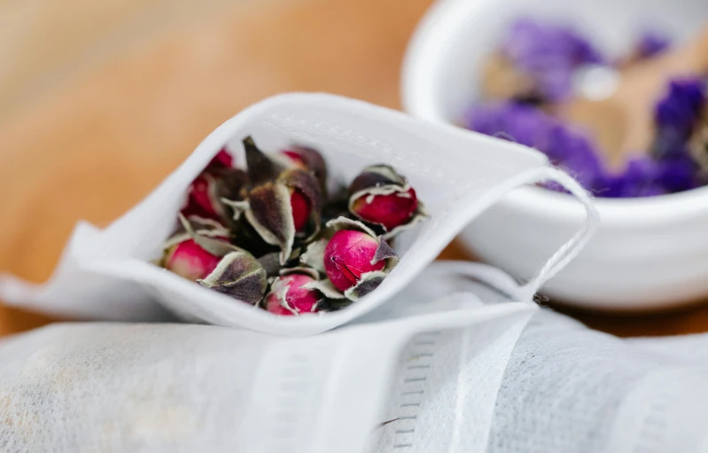 two white bowls filled with flowers on top of a wooden table, inspired by Annie Rose Laing, unsplash, black and purple rose petals, teapots, parchment paper, silver white red details