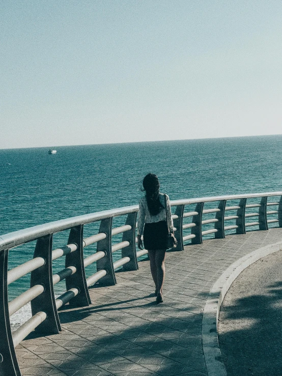 a woman walking down a walkway next to the ocean, profile image, set on singaporean aesthetic, crossing the blue horizon, the emerald coast