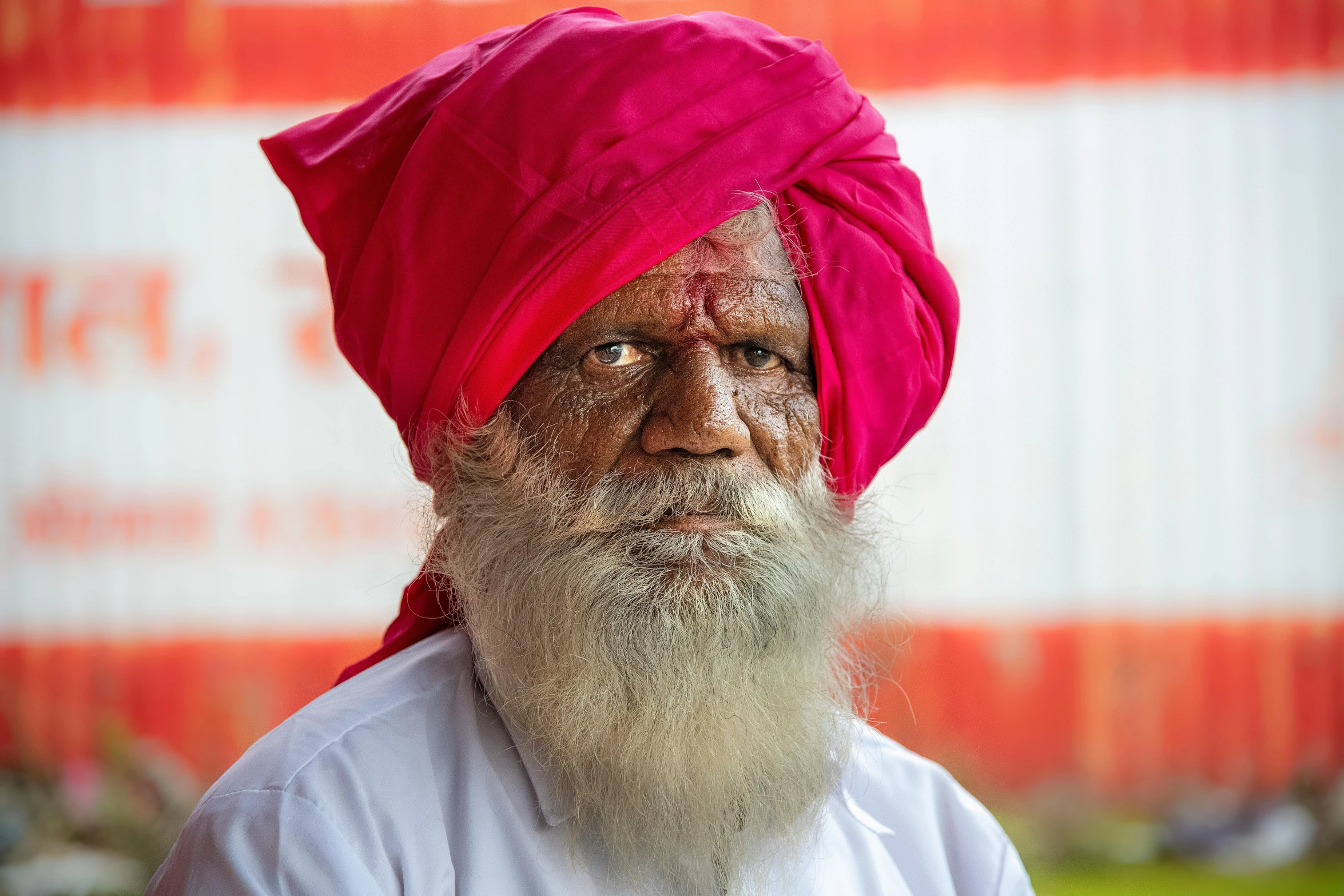 a man with a long beard wearing a pink turban, by Bapu, pexels contest winner, samikshavad, dwarf with white hair, red birthmark, slightly pixelated, portrait of an old