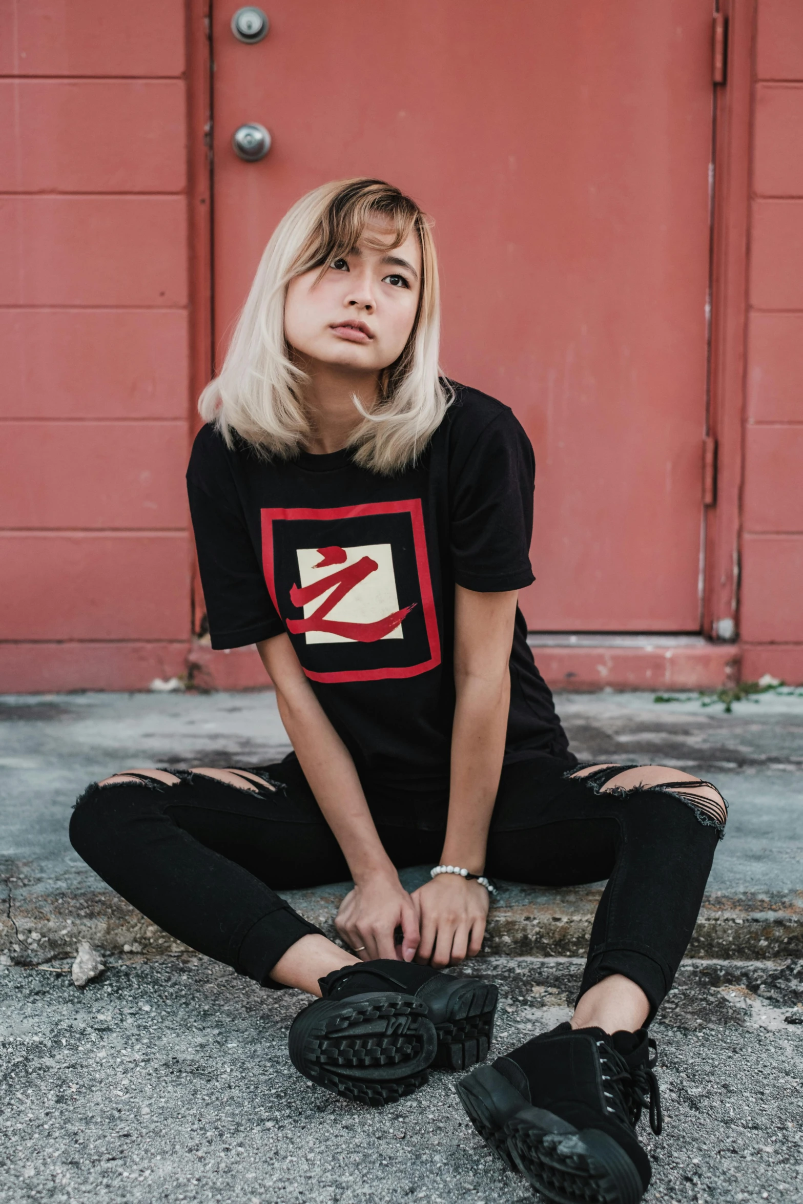 a woman sitting on the ground in front of a red door, a cartoon, inspired by Zhu Da, featured on instagram, graffiti, black t shirt, x logo, indonesia, smol