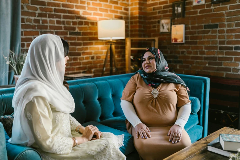 a couple of women sitting on top of a blue couch, a portrait, unsplash, hurufiyya, robed figures sat around a table, wearing a head scarf, sitting on a mocha-colored table, talking