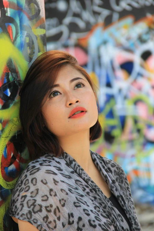 a woman leaning against a graffiti covered wall, an album cover, inspired by Elaine Duillo, pexels contest winner, toyism, south east asian with round face, lipstick, blurred, leni robredo