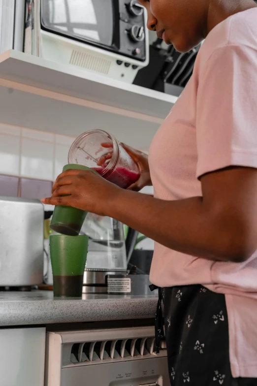 a woman making a smoothie in a kitchen, by Sam Charles, pexels, pink and green, dark-skinned, made of liquid, plating