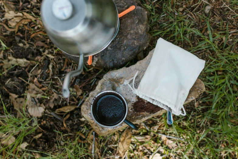 a kettle sitting on top of a rock next to a cup of coffee, by Julian Allen, bags on ground, drip, recipe, detail shot