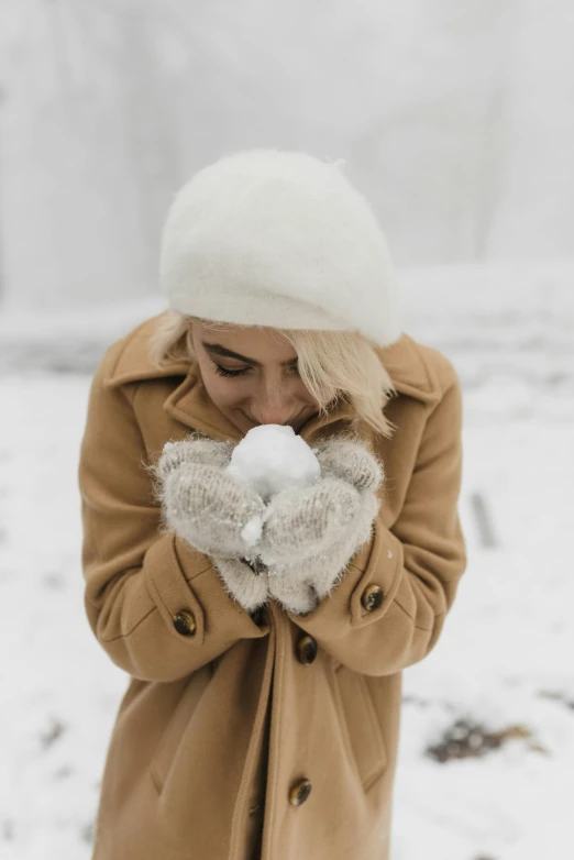 a woman standing in the snow wearing a coat and mittens, inspired by Elsa Bleda, trending on pexels, holding a white duck, hat covering eyes, puffballs, gif