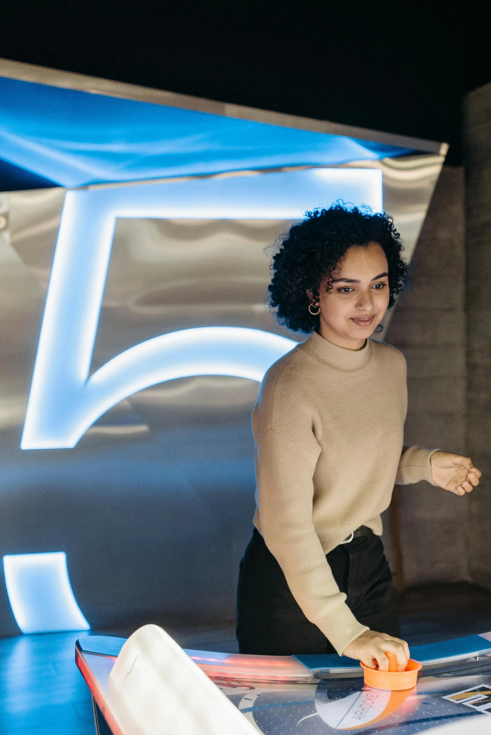 a woman that is standing in front of a table, trending on unsplash, unreal engine 5 lighting, dark short curly hair smiling, 5 th floor, neon electronic signs
