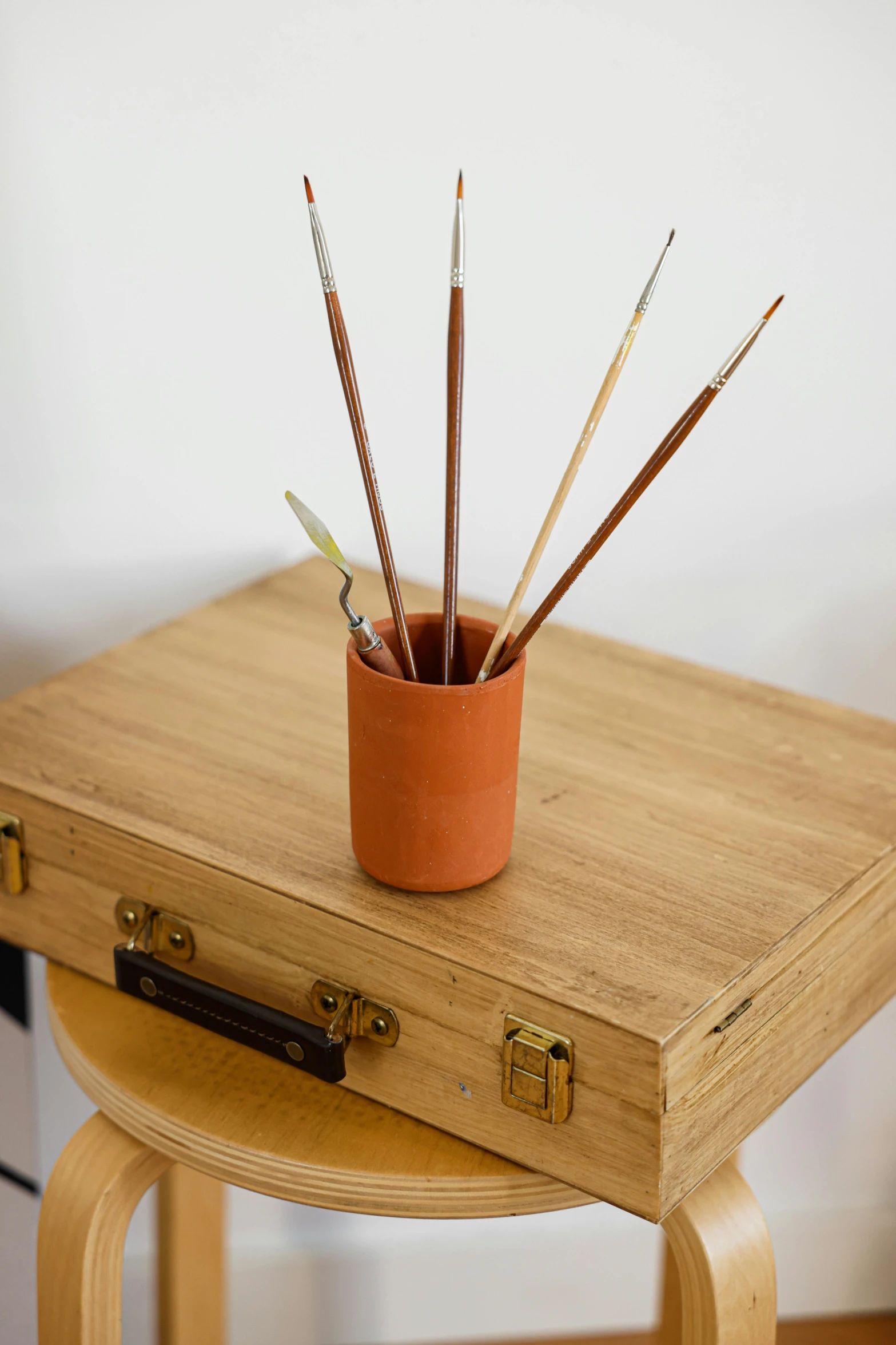 a piece of luggage sitting on top of a wooden table, a minimalist painting, inspired by Hendrik Gerritsz Pot, unsplash, holding paintbrushes, terracotta, set against a white background, detail shot