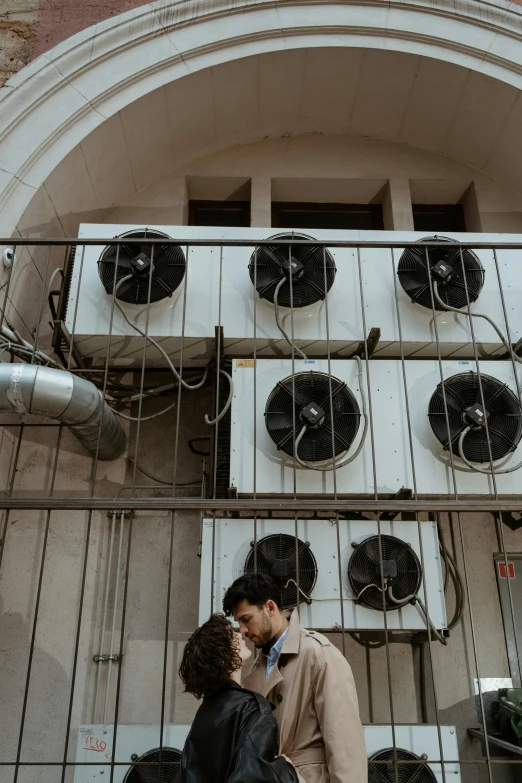 a couple standing next to each other in front of a building, by Jacob de Heusch, pexels contest winner, renaissance, air conditioner, kissing, electricity archs, stacked