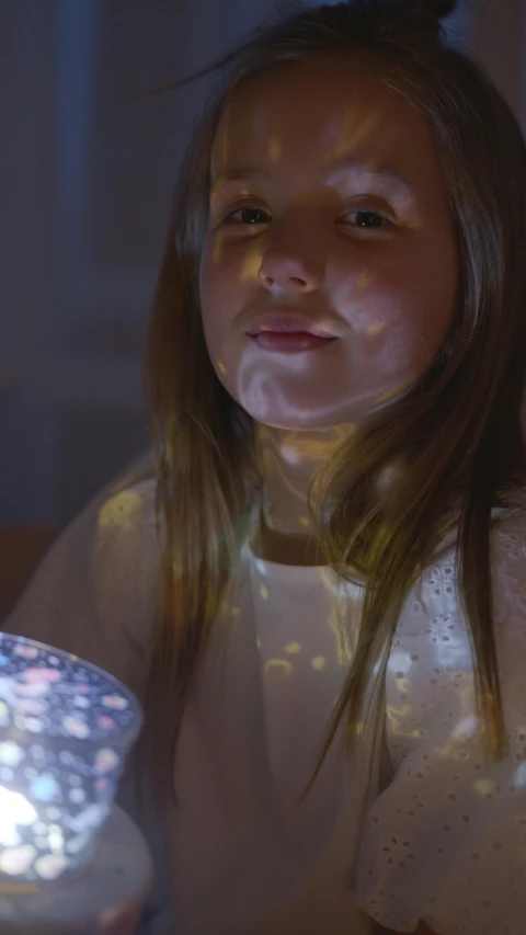 a little girl that is sitting in front of a cake, a hologram, pexels, interactive art, emerging from her lamp, close-up portrait film still, intricate 8 k detail, in the bedroom at a sleepover
