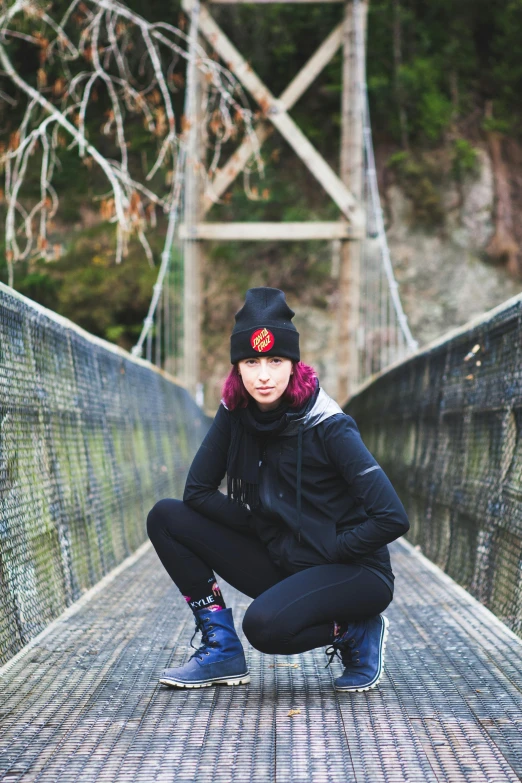 a woman squatting down on a bridge, a portrait, inspired by Kaii Higashiyama, unsplash, black beanie, black widow, wearing adventure gear, coloured photo