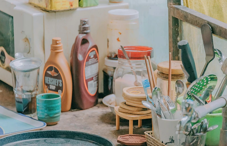 a kitchen counter filled with dishes and utensils, unsplash, photorealism, bottles covered in wax, 90s photo, brown, bright daylight indoor photo