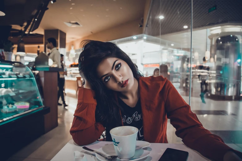 a woman sitting at a table with a cup of coffee, a picture, inspired by Elsa Bleda, trending on pexels, beautiful iranian woman, teenage girl, red, cinematic outfit photo