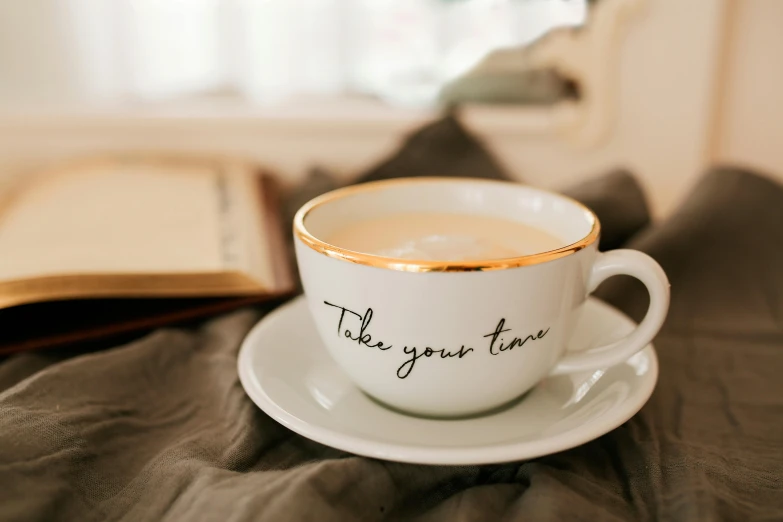 a cup of coffee and a book on a bed, trending on pexels, tachisme, inspirational quote, thin porcelain, golden time, in a white boho style studio