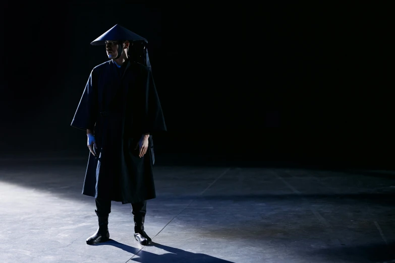 a man in a cap and gown standing in a dark room, inspired by Yukihiko Yasuda, unsplash, conceptual art, fashion show photo, hito steyerl, ground - level medium shot, hanfu