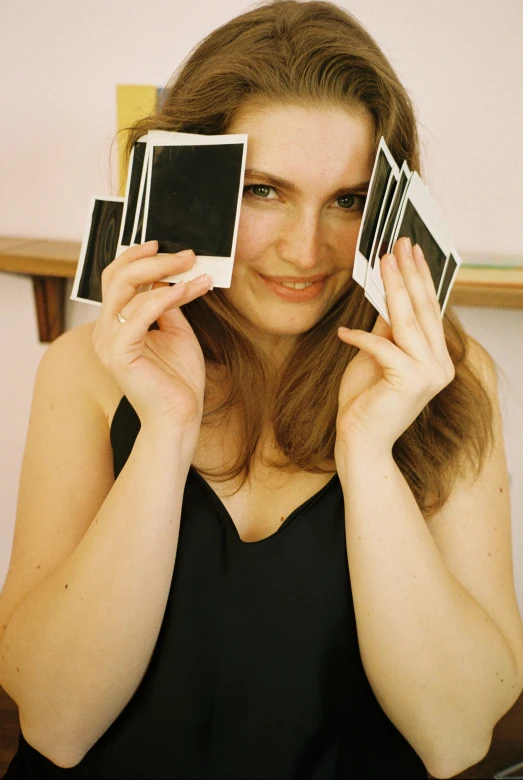 a woman holding up two polaroids in front of her face, inspired by Anna Füssli, happening, natalie portman, cardistry, press shot, ( ( photograph ) )