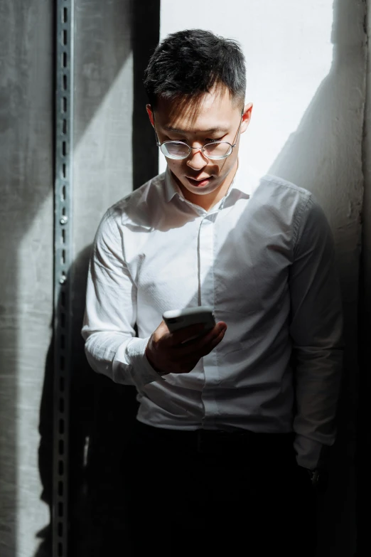 a man in a white shirt looking at his cell phone, inspired by Cheng Jiasui, trending on pexels, posing in dramatic lighting, in data center, outfit photograph, with glasses