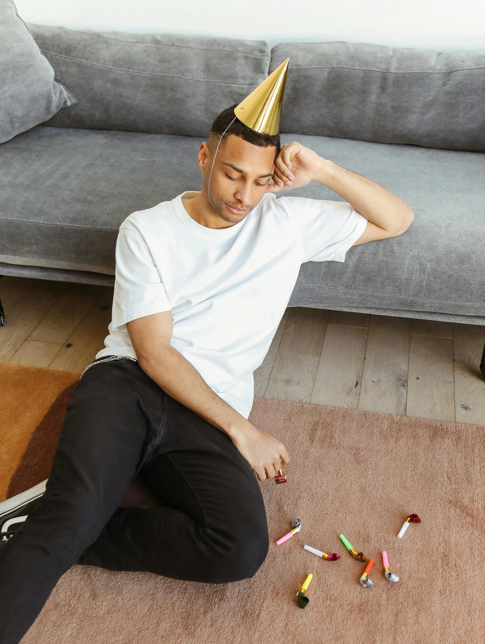 a man sitting on the floor wearing a party hat, trending on unsplash, happening, sleepy expression, gold shirt, lean man with light tan skin, with furniture overturned