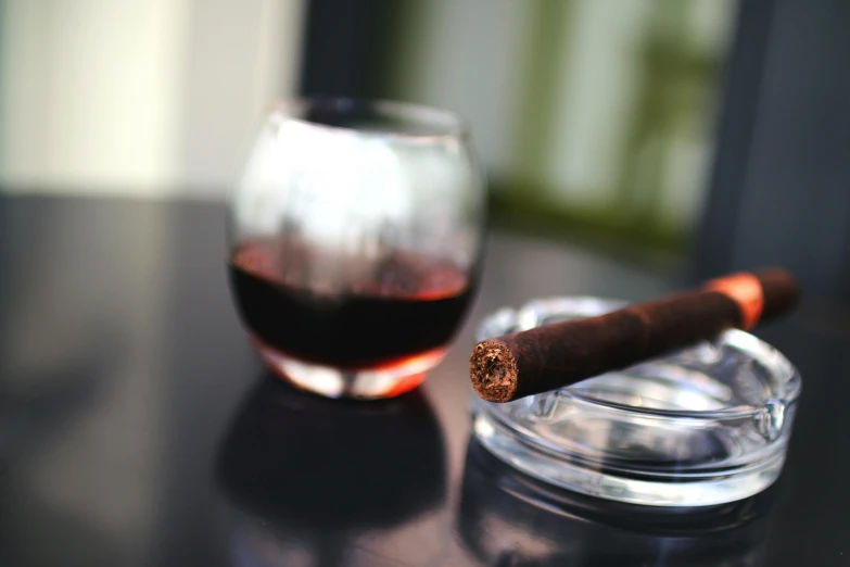 a glass of wine and a cigar on a table, with an ashtray on top, thumbnail, slightly out of focus, half turned around