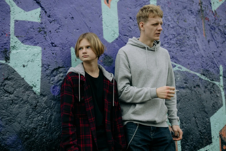 a man and a woman standing in front of a graffiti wall, an album cover, pexels, blond boy, brothers, tv series, boyish