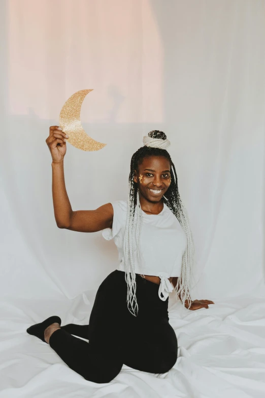 a woman sitting on a bed holding a paper bird, by Dulah Marie Evans, trending on unsplash, afrofuturism, in front of a big moon, posing in leotard and tiara, while smiling for a photograph, photo booth