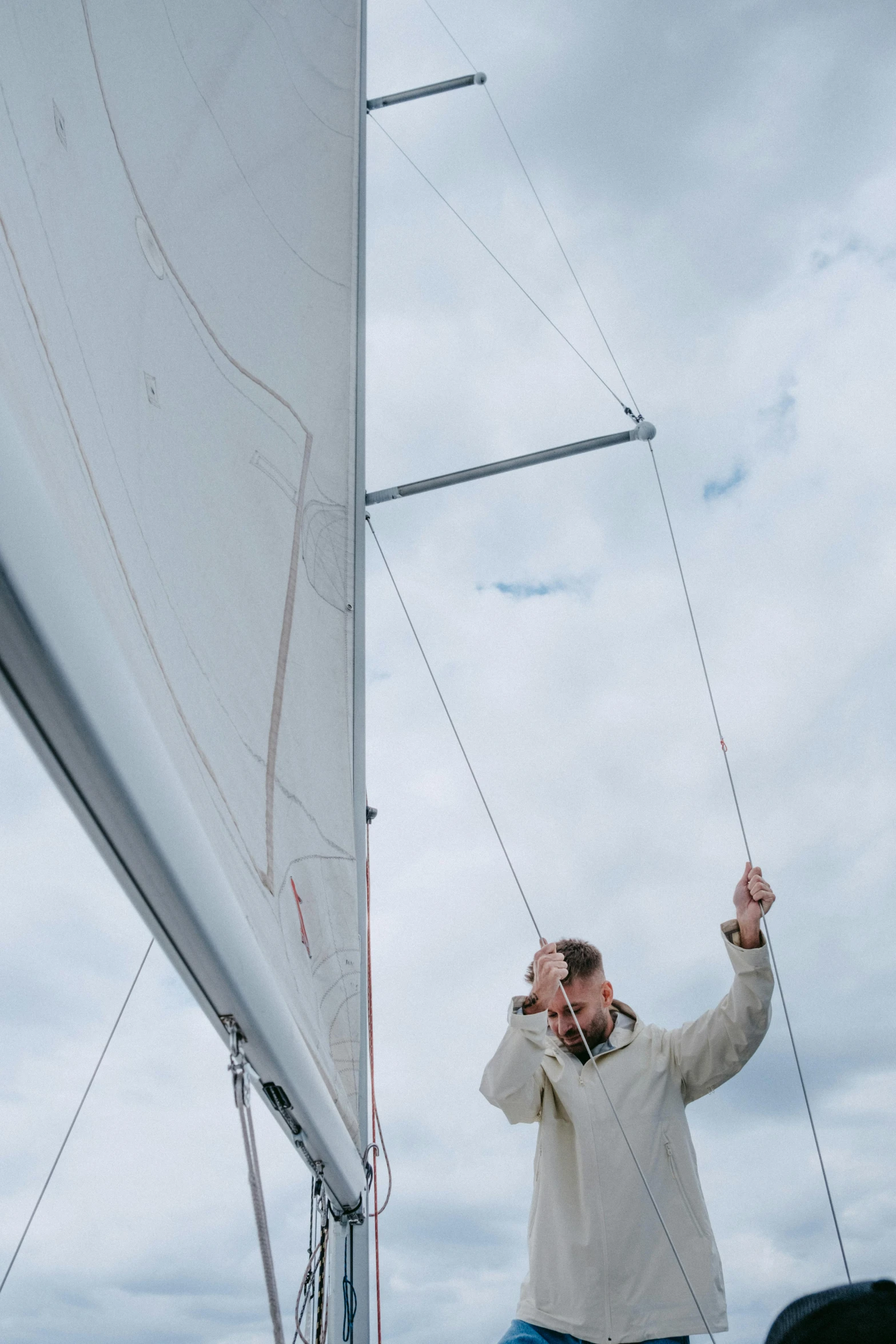 a man that is standing on a boat, sailing boat, looking up onto the sky, grey, bending down slightly