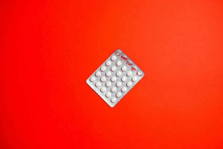 a pill pack sitting on top of a red surface, by Carey Morris, trending on pexels, plasticien, square, made of dots, aluminum, white and orange