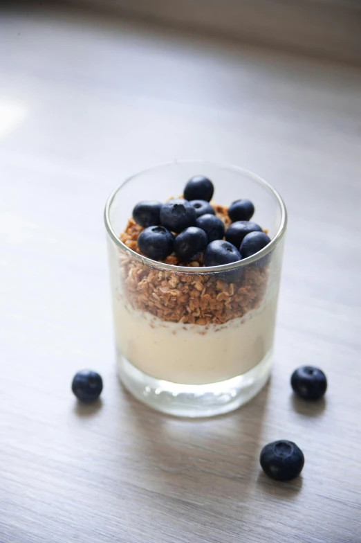 a glass filled with blueberries on top of a wooden table, sea of parfait, crispy, on grey background, manuka