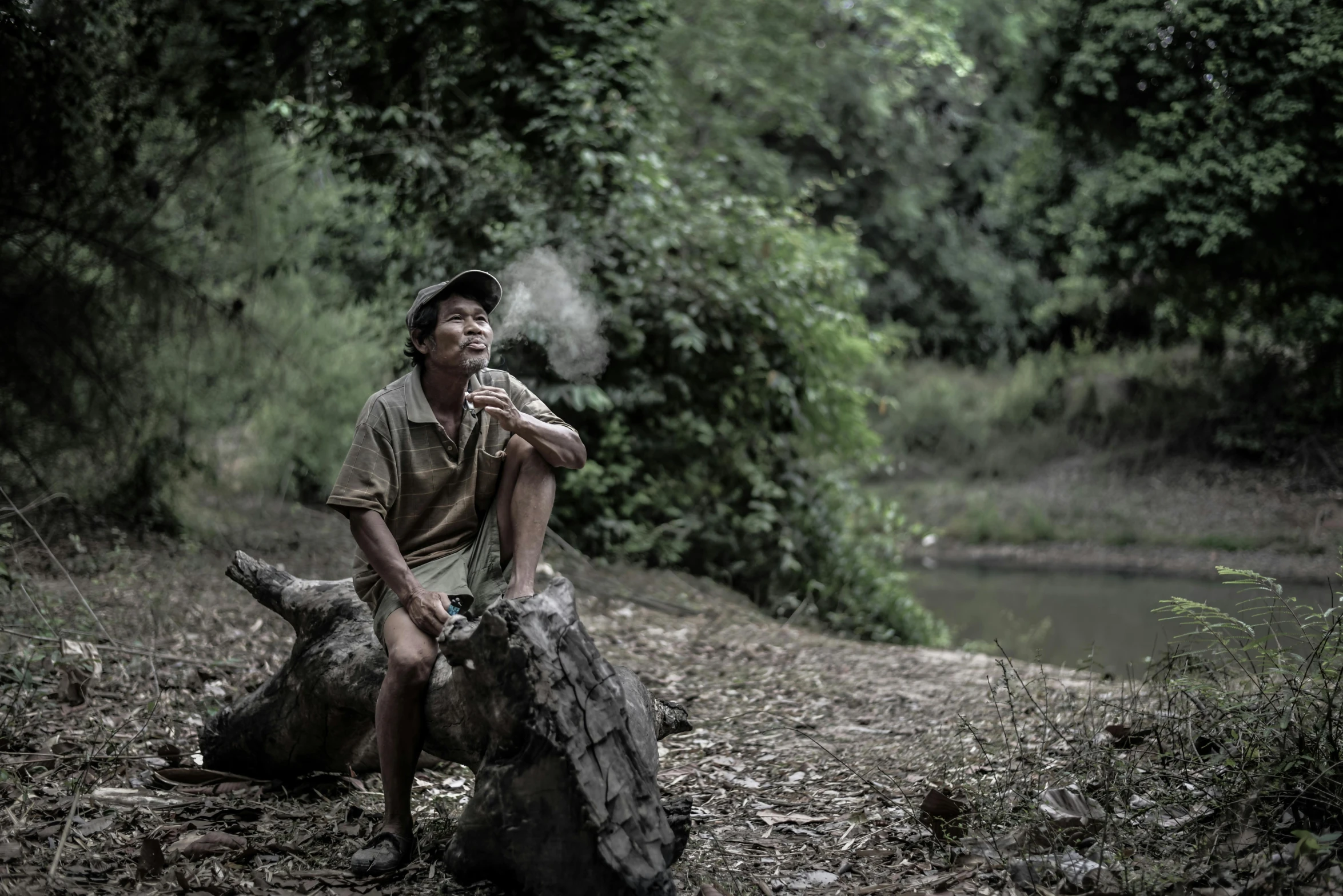 a man sitting on a log smoking a cigarette, by Peter Churcher, pexels contest winner, sumatraism, forest picnic, aboriginal capirote, on a riverbank, immature