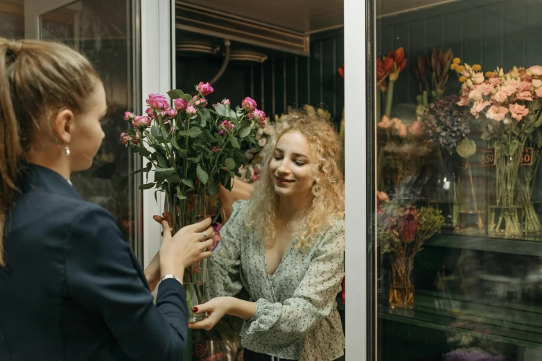 a woman standing in front of a window holding a bunch of flowers, pexels contest winner, exiting store, smiling at each other, mid 2 0's female, alana fletcher