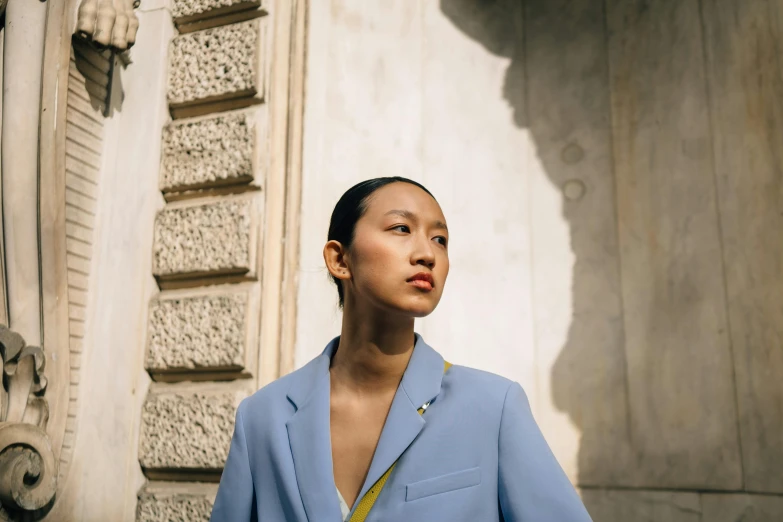 a woman in a blue suit standing in front of a building, inspired by Wang Lü, trending on pexels, light grey blue and golden, demna gvasalia, asian descent, paris fashion week