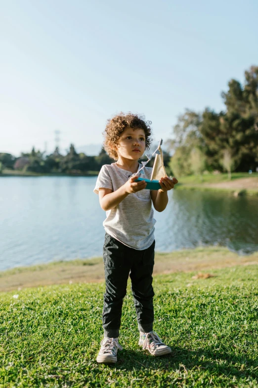 a little boy standing on top of a lush green field, pexels contest winner, graffiti, wielding a fish sword, in a park and next to a lake, paper airplane, mini model